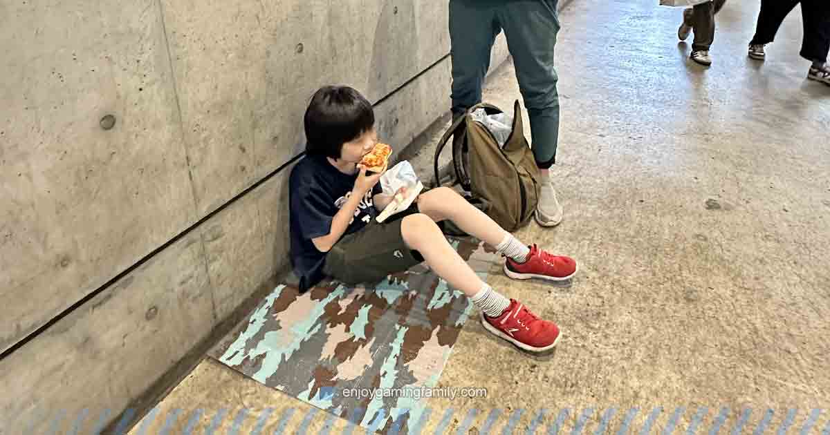 東京ゲームショウ2024の会場通路で、レジャーシートに座ってパンを食べる子供。