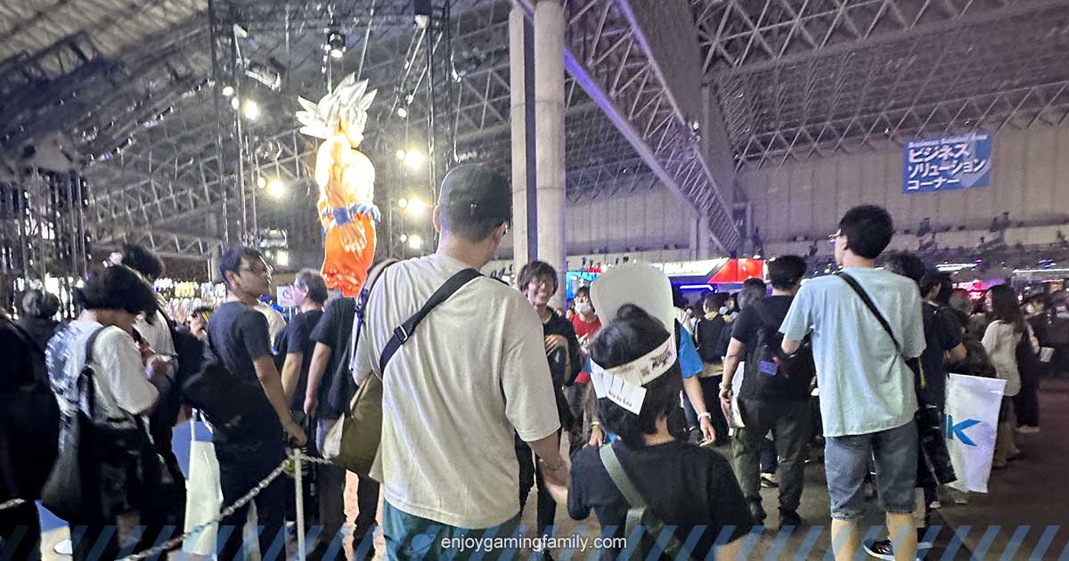東京ゲームショウ2024の会場内、ドラゴンボールの巨大な悟空バルーンが見える展示エリア。父親と子どもが手をつないで歩いており、混雑する通路の様子がわかる。
